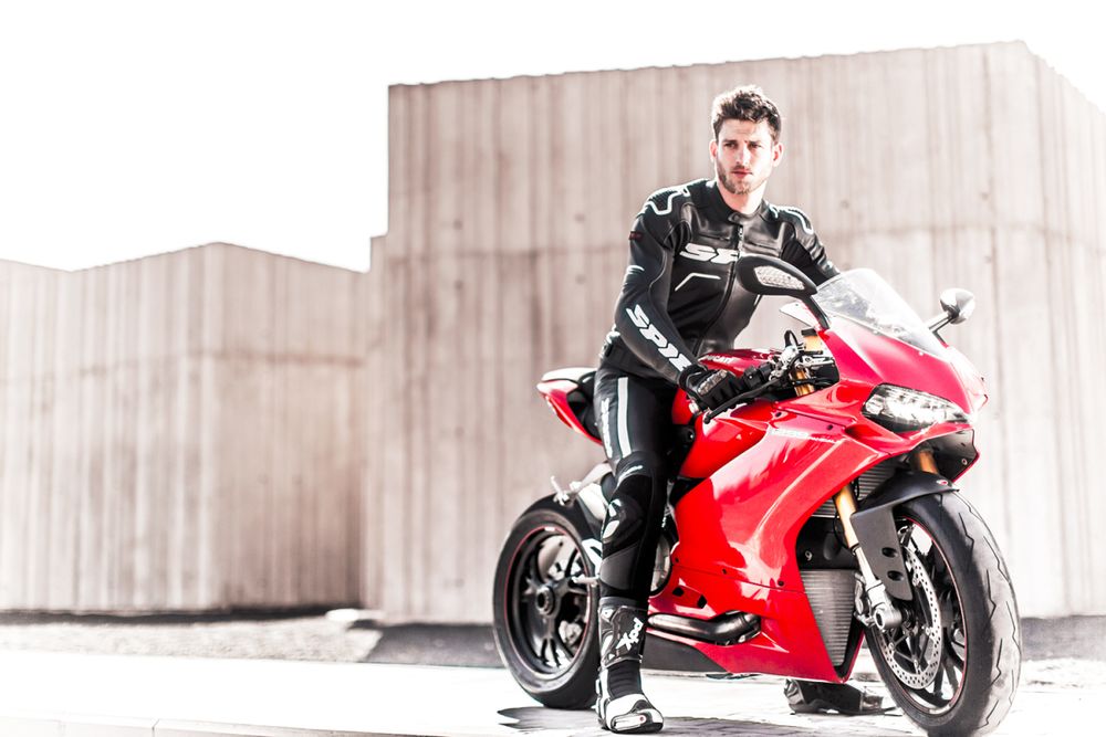 نمایه ای از یک مرد جوان با لباس موتورسواری مشکلی که سوار بر موتور قرمز رنگ