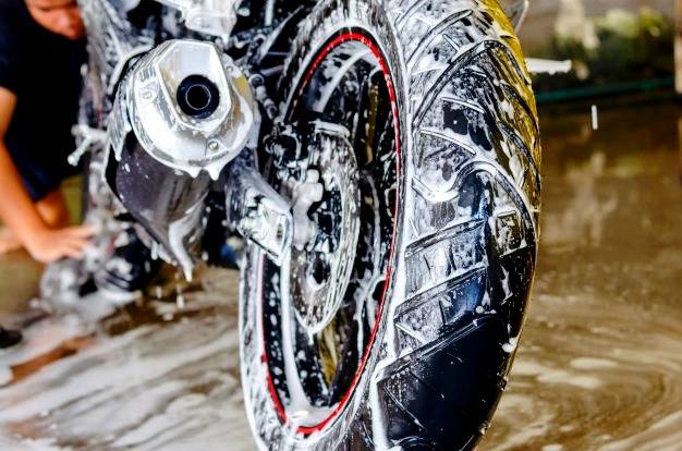 عکسی از تایر عقب و لوله اگزوز موتور سیکلت که روی آن مایع شست و شو و یه عالمه کف شست و شو قرار دارد 