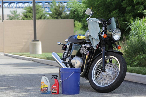 تصویری از موتورسیکلتی که پارک شده و کنارش سطل آب اسپری و مایع شوینده قرار دارد روی یکی از آینه ها هم یک دستمال تنظیف قرار گرفته